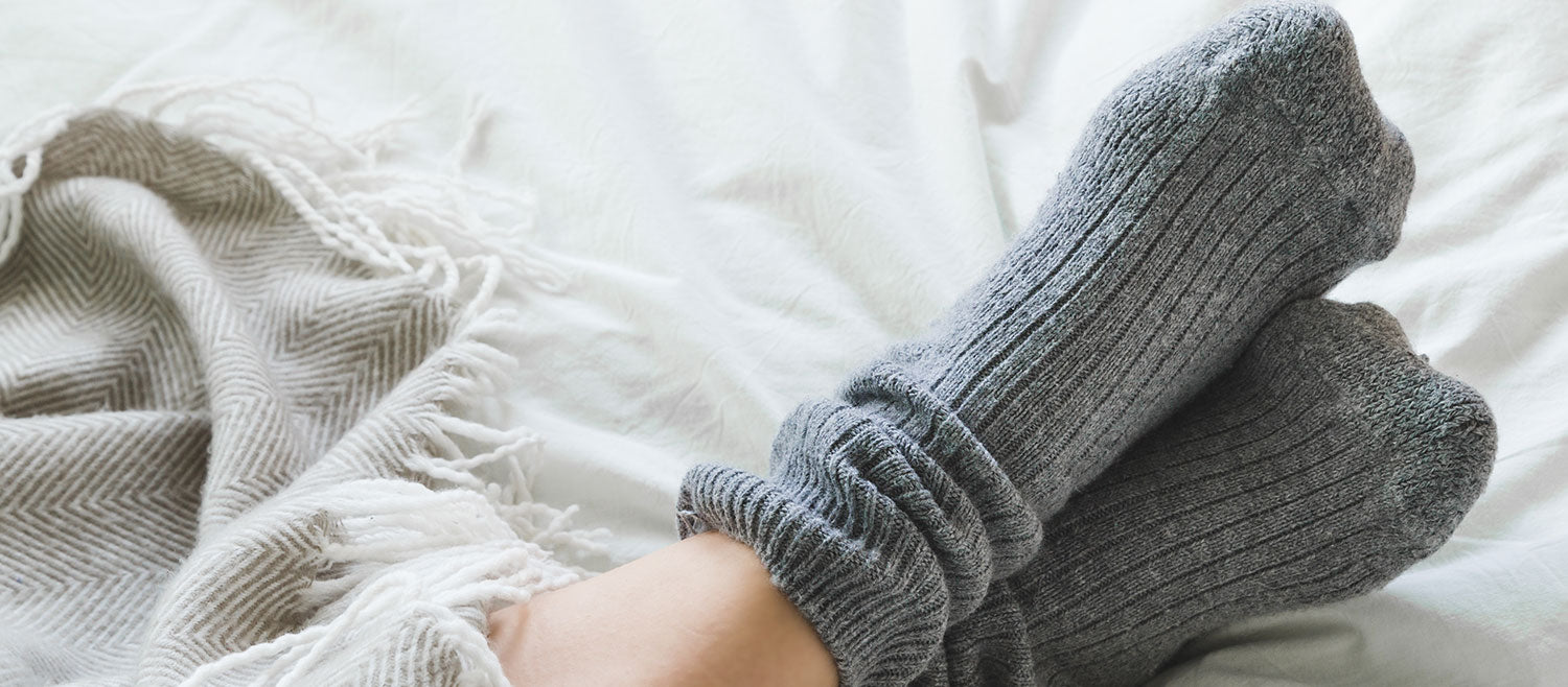 A close-up of a person’s feet wearing cozy gray socks in bed