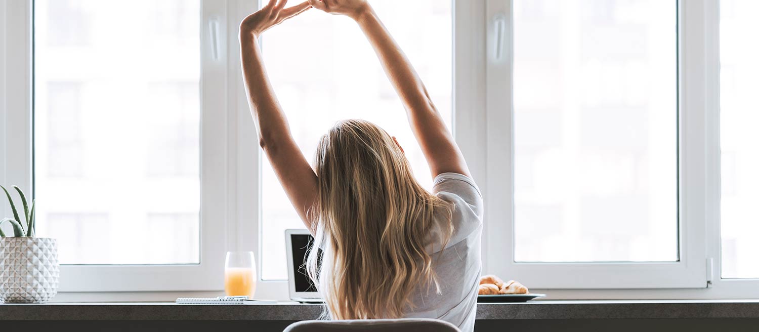 Blonde haired women wearing a white T-shirt trying different desk stretches while working from home