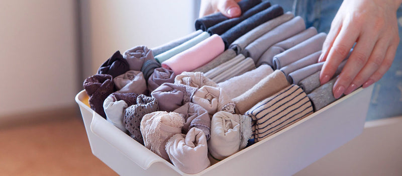 Close-up of a white container of rolled and folded underwear and lace panties of different colors and styles