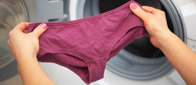 Woman with pink nail polish holding up maroon colored underwear about to toss it into her washing machine