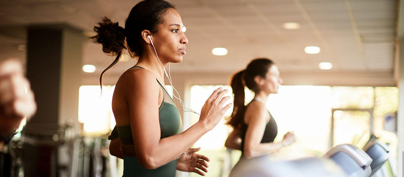 A woman running on a treadmill at the gym while wearing wired headphones